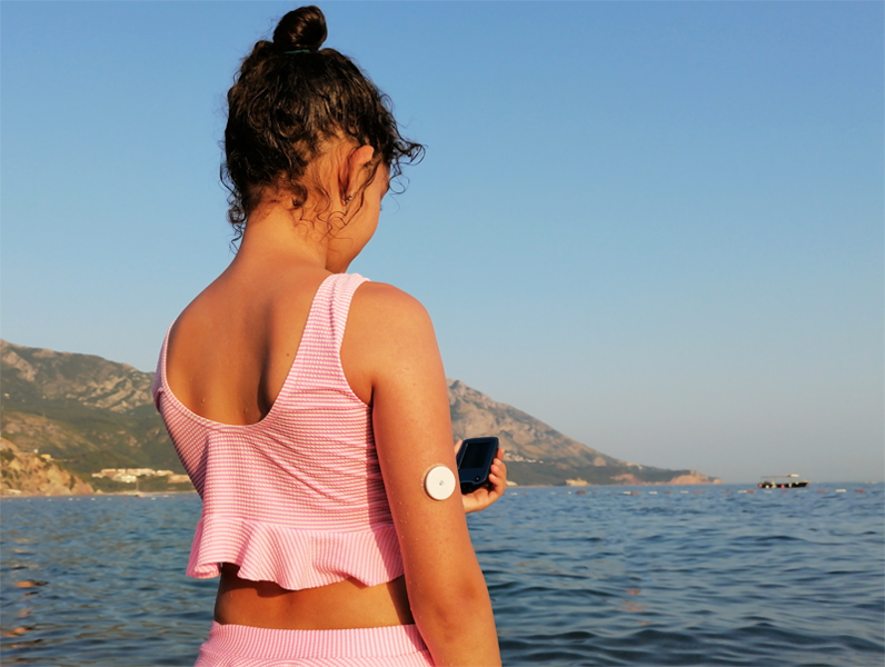 Girl with CGM on arm by the sea. 